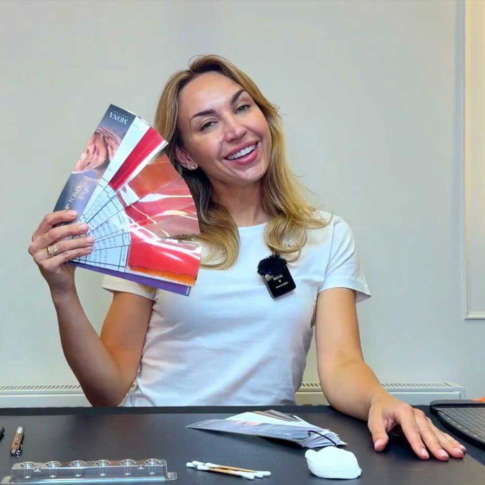 PMU Artist Ramona holding up her color swatch cards while sitting at a desk
