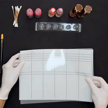 Gloved hands holding a pigment swatch grid with PMU pigments, pigment cup tray, and cotton swabs.