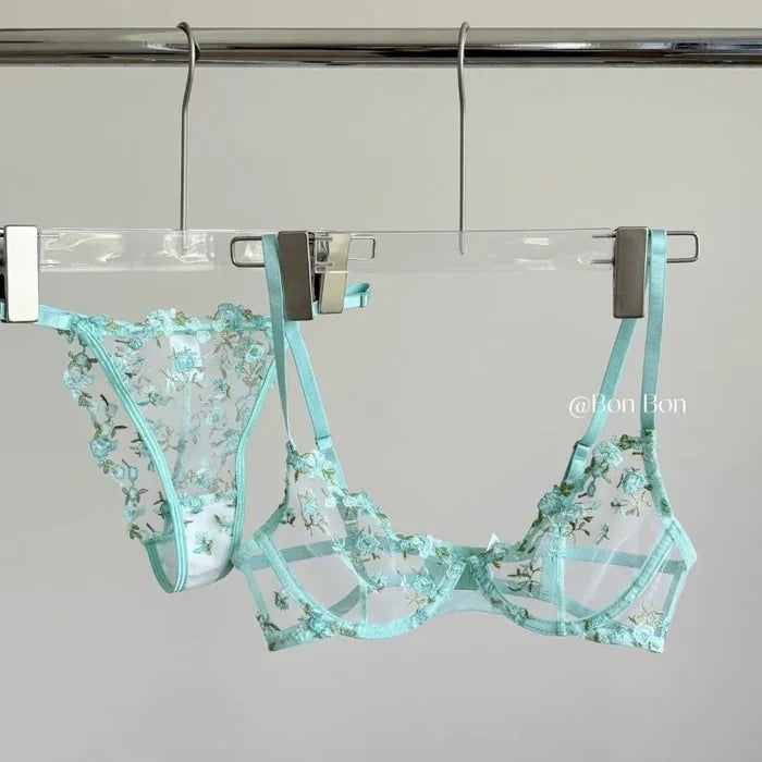 Teal floral lingerie set hanging on a rack against a gray background