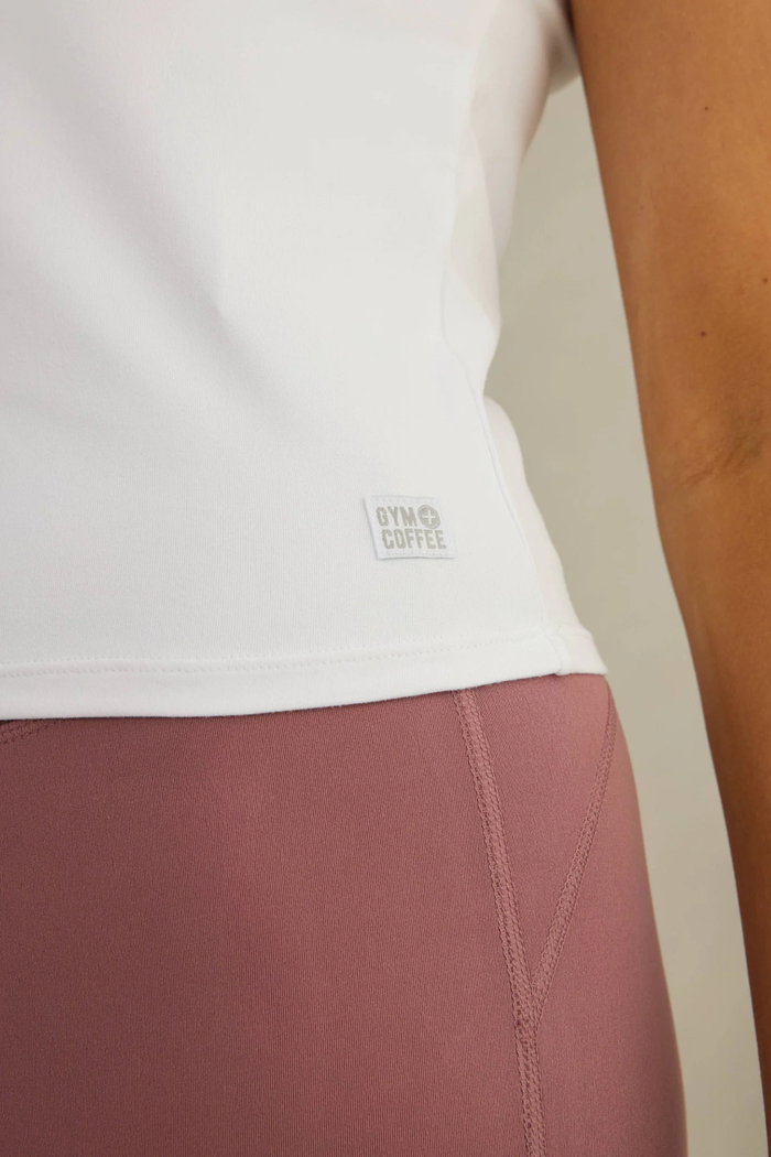 Close-up of the Gym+Coffee Daily Urban Tee in Ultra White worn with mauve leggings, shop Gym+Coffee at Dotique.