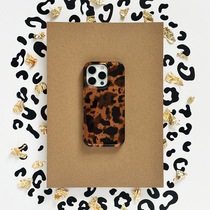 Coconut Lane Leopard Tort phone case with black spots and gold foil accents on a brown paper background.