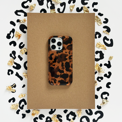 Coconut Lane Leopard Tort phone case with black spots and gold foil accents on a brown paper background.