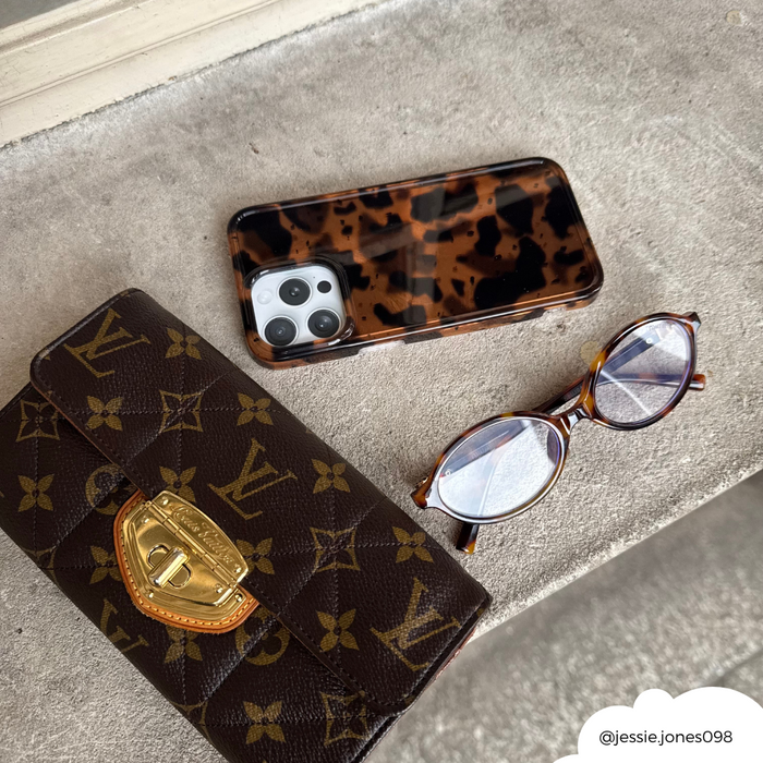 Monogram Louis Vuitton wallet, leopard print tortoiseshell phone case, and oval tortoiseshell glasses on gray surface.